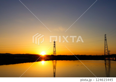 夕陽と水を張った田んぼに映る鉄塔のリフレクション風景 124615445