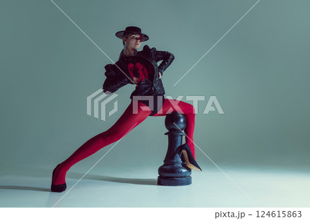 Mysterious woman in structured black outfit and red tights leans over chess piece, evoking authority. Concept of balance 124615863