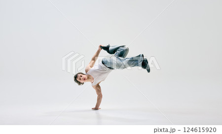 Skilled b-boy, dressed casually, executing powerful aerial move, seamlessly merging art and sport against white background. 124615920