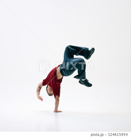 Young breakdancer flipping mid-air, his body arched against white studio background, motion captured in perfect form. 124615954