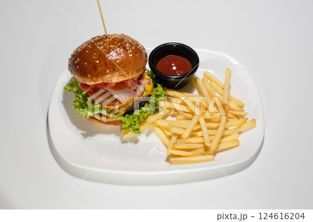 Delicious Classic Hamburger with Crispy French Fries and Fresh Vegetables on White Plate with Tomato Sauce 124616204