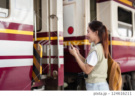 Traveling and Adventure. A young traveler checks her smartphone while waiting at the train station. 124616211