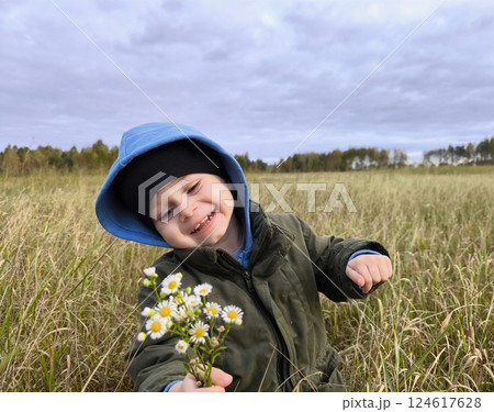 A happy child in a flower field. A child with a bouquet of flowers. A boy in a flower meadow with a bouquet of daisies. An outdoor nature park. A child with flowers in his hands 124617628
