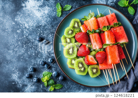 A colorful platter of fresh fruit skewers with vibrant slices of watermelon, kiwi, and strawberries arranged neatly 124618221