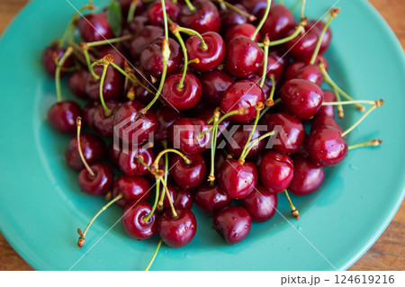 A vibrant pile of ripe red cherries sits on a teal plate, showcasing their juicy freshness A vibrant pile of ripe red cherries sits on a teal plate, showcasing their juicy freshness 124619216