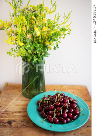 A vibrant summer still life featuring a bouquet of yellow wildflowers and a bowl of ripe red cherries on a rustic wooden table A vibrant summer still life featuring a bouquet of yellow wildflowers and a bowl of ripe red cherries on a rustic wooden table 124619217