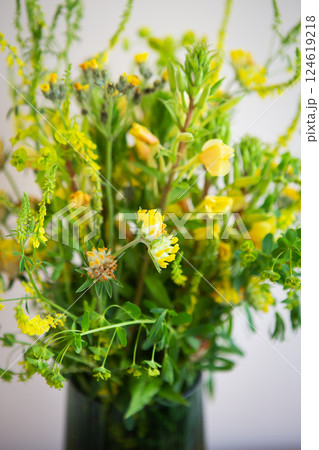 A vibrant bouquet of wildflowers in yellow and green hues fills a dark vase, creating a cheerful summer scene A vibrant bouquet of wildflowers in yellow and green hues fills a dark vase, creating a cheerful summer scene 124619218