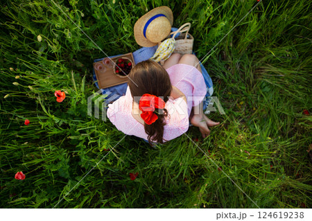 A young woman enjoys a tranquil picnic amidst a vibrant poppy field, surrounded by nature's beauty 124619238