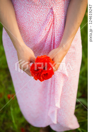 A woman in a pink patterned dress gently holds a vibrant red poppy flower bouquet in her hands 124619247