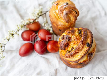 Freshly baked pastries beside red eggs and delicate white flowers, displayed on a textured fabric. 124619254