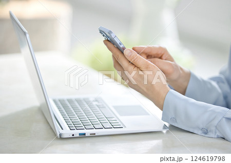 リビングでパソコンを見ながらスマホを操作するミドル女性 124619798