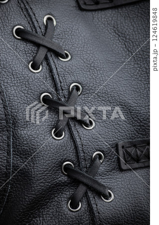 Close-Up of Black Leather Jacket Lacing. This image shows a close-up of the decorative lacing detail on the side of the black leather sleeveless jacket. Black laces are threaded through silver Close-Up of Black Leather Jacket Lacing. This image shows a close-up of the decorative lacing detail on the side of the black leather sleeveless jacket. Black laces are threaded through silver 124619848