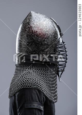 Dark Helmet with Ribbed Faceplate and Chainmail. This image shows a dark, possibly blackened steel, helmet with a pointed top and a distinctive faceplate featuring a series of horizontal ribs. A Dark Helmet with Ribbed Faceplate and Chainmail. This image shows a dark, possibly blackened steel, helmet with a pointed top and a distinctive faceplate featuring a series of horizontal ribs. A 124619863