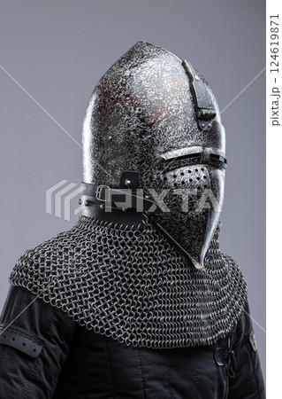 Dark Metal Helmet with Pointed Top and Faceplate. This image shows a dark metal helmet with a pointed top and a faceplate that covers the lower part of the face, featuring several horizontal slits for 124619871
