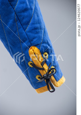 Blue Quilted Sleeve with Yellow Trim and Black Lacing. This image shows a close-up of a blue quilted sleeve with yellow edging and black laces threaded through yellow loops. Blue Quilted Sleeve with Yellow Trim and Black Lacing. This image shows a close-up of a blue quilted sleeve with yellow edging and black laces threaded through yellow loops. 124620077