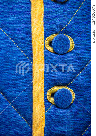 Detailed View of Blue Quilted Textile with Yellow Accents. This close-up showcases the texture of blue quilted fabric featuring a vertical yellow strip and two round blue buttons with yellow Detailed View of Blue Quilted Textile with Yellow Accents. This close-up showcases the texture of blue quilted fabric featuring a vertical yellow strip and two round blue buttons with yellow 124620078