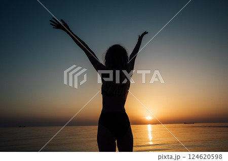 Silhouette of slender woman with hands up in the sea at sunset Silhouette of slender woman with hands up in the sea at sunset 124620598