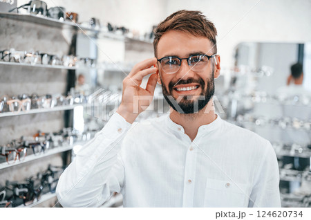 Cheerful mood. Stylish man with beard choosing glasses in the optics store Cheerful mood. Stylish man with beard choosing glasses in the optics store 124620734