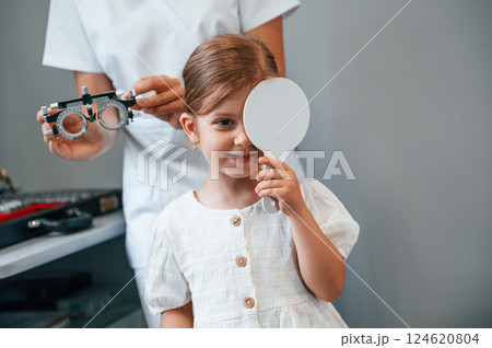Covering left eye. Little girl have their vision checking in the clinic by help of the female doctor Covering left eye. Little girl have their vision checking in the clinic by help of the female doctor 124620804