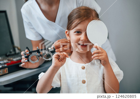 Covering left eye. Little girl have their vision checking in the clinic by help of the female doctor 124620805