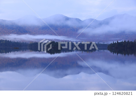 紅葉の山に囲まれた水辺に霧が流れ水墨画の世界 124620821