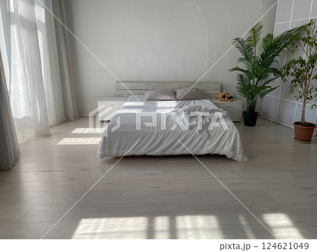 Interior of a white bedroom with a bed and green plants by the window 124621049