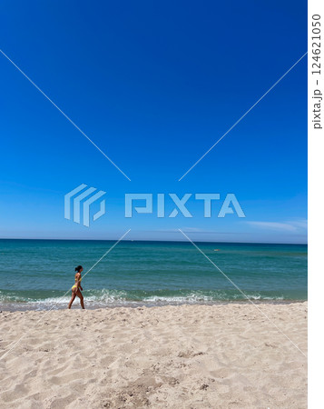 Woman in swimsuit walking along sandy beach by blue sea 124621050