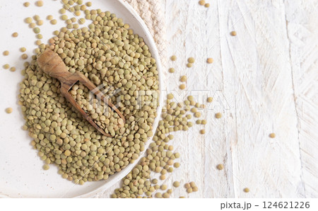 Plate full of dried raw green lentils with a wooden scoop on white table top view. Vegetarian food 124621226