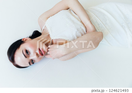 Beautiful brunette woman bride in white dress lying in bedroom Beautiful brunette woman bride in white dress lying in bedroom 124621493
