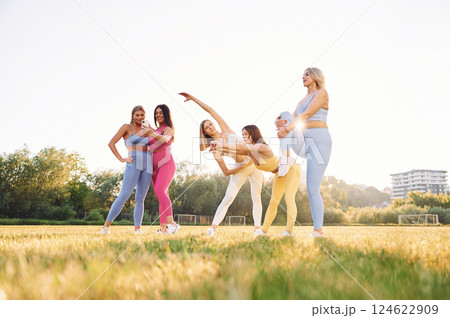 Standing and practicing. Group of women have fitness outdoors on the field together 124622909