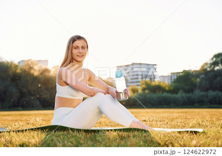 Sitting on the ground, posing and resting. Beautiful woman in sportive clothes doing fitness exercises outdoors on the field 124622972