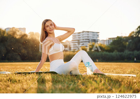 Sitting on the ground, posing and resting. Beautiful woman in sportive clothes doing fitness exercises outdoors on the field Sitting on the ground, posing and resting. Beautiful woman in sportive clothes doing fitness exercises outdoors on the field 124622975