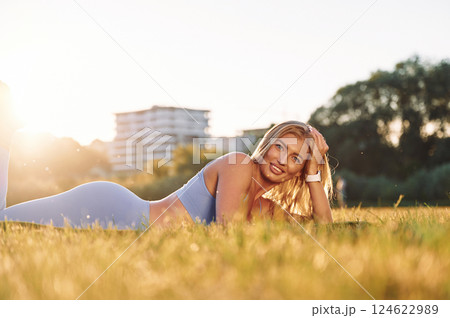 In blue clothes. Laying down on the ground. Beautiful woman in sportive clothes doing fitness exercises outdoors on the field In blue clothes. Laying down on the ground. Beautiful woman in sportive clothes doing fitness exercises outdoors on the field 124622989