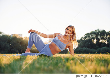 Laying down on the ground. Beautiful woman in sportive clothes doing fitness exercises outdoors on the field 124622992