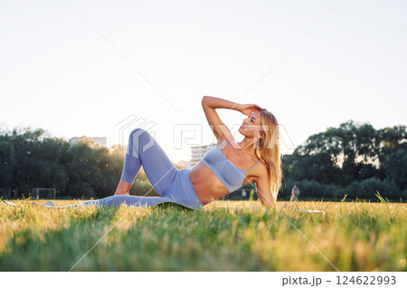 Laying down on the ground. Beautiful woman in sportive clothes doing fitness exercises outdoors on the field 124622993