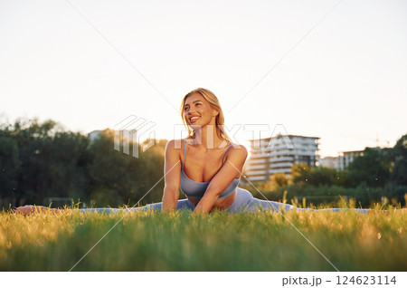 Stretching the legs. Beautiful woman in sportive clothes doing fitness exercises outdoors on the field Stretching the legs. Beautiful woman in sportive clothes doing fitness exercises outdoors on the field 124623114