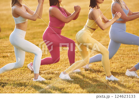 Doing legs exercises. Group of women have fitness outdoors on the field together 124623133