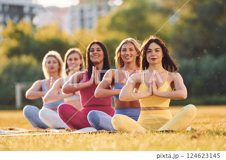 Calm meditation in lotus pose. Group of women have fitness outdoors on the field together Calm meditation in lotus pose. Group of women have fitness outdoors on the field together 124623145