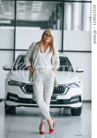 Standing and posing. Woman in white formal clothes is in the car dealership 124623338
