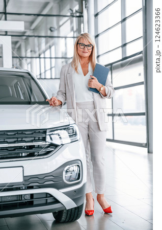Manager is ready to help. Woman in white formal clothes is in the car dealership 124623366