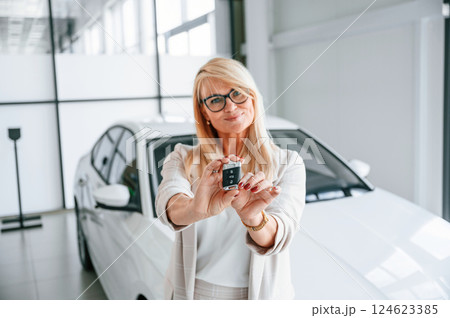Holding keys. Woman in white formal clothes is in the car dealership 124623385