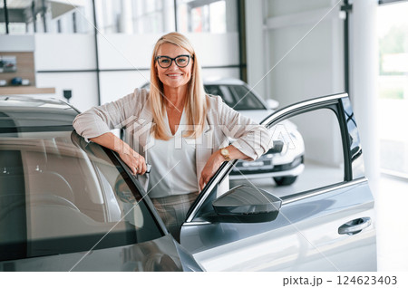 Happy positive woman in white formal clothes is in the car dealership 124623403