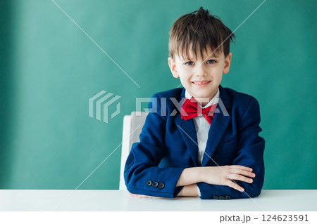Schoolboy Boy In Business Suit Sitting At Table And Smiling Schoolboy Boy In Business Suit Sitting At Table And Smiling 124623591