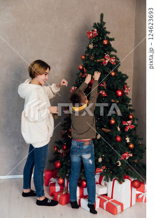 Mom and son decorating Christmas tree with gifts for the new year with balloons Mom and son decorating Christmas tree with gifts for the new year with balloons 124623693