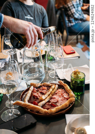 Wine being poured at a table set with tasting cards, cured meats, and glassware during a group event. Wine workshop, communal tasting, food and wine pairing, social gathering 124624982