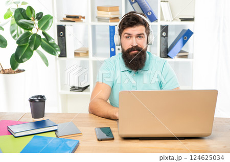 Serious man listening to webinar in headphones using laptop in office, online education 124625034