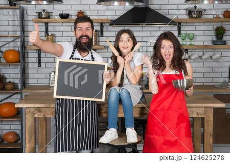 parents with daughter cooking at home. girl help mother and father. Family traditions. family preparing meal in kitchen together. mom dad and kid hold blackboard. spend free time together. copy space 124625278