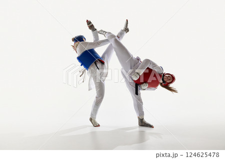 Competitive young women, taekwondo fighters in dynamic motion, training against studio background. 124625478