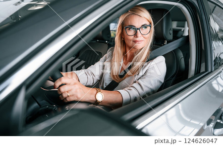 Driving new automobile. Woman in white formal clothes is in the car dealership 124626047