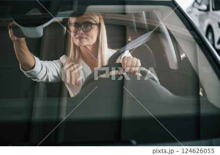 Front view. Woman in white formal clothes is in the car dealership 124626055